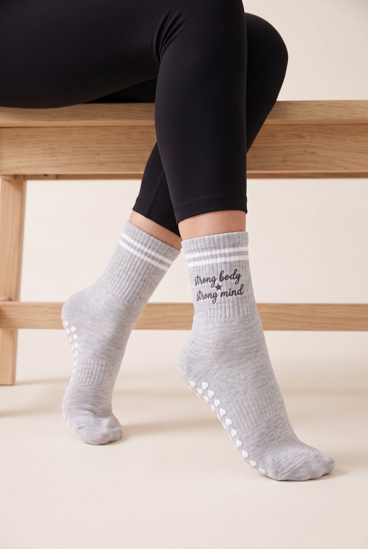 Model wearing grey crew pilates grip socks beside a studio bench
