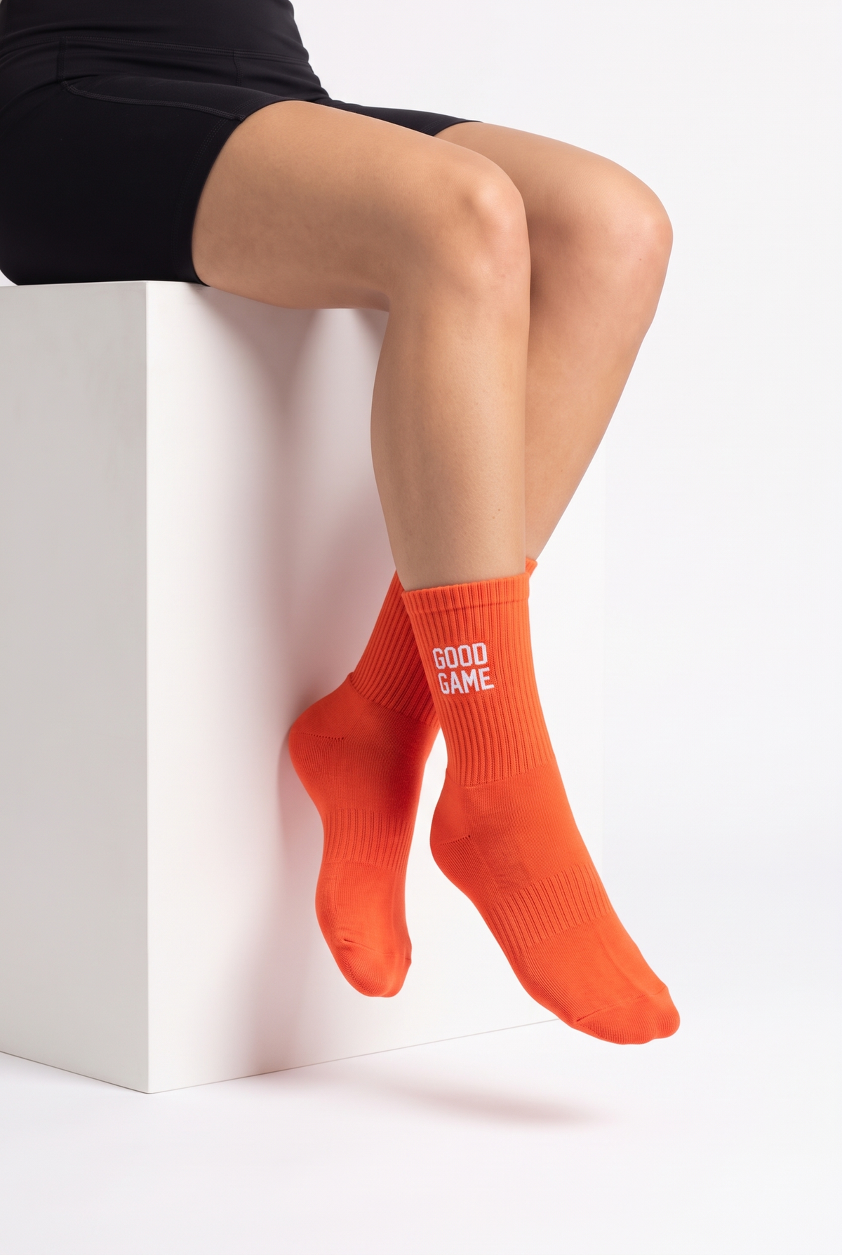 Model wearing orange embroidered tennis socks, seated