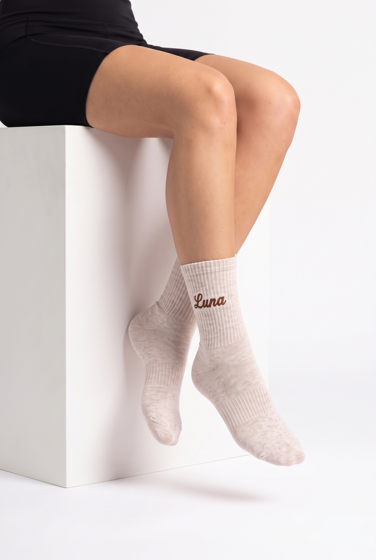 Model wearing cream melange embroidered tennis socks, seated