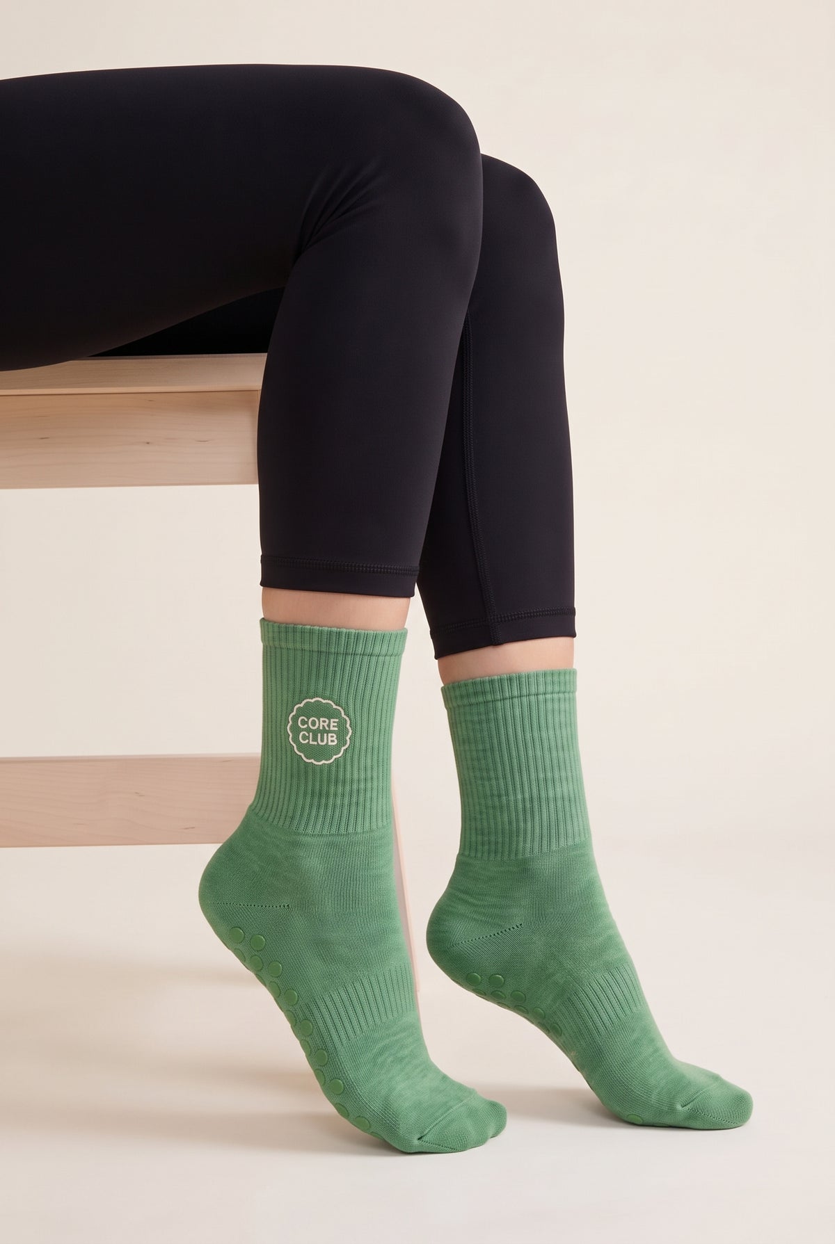 Model wearing green embroidered dot grip pilates socks, seated