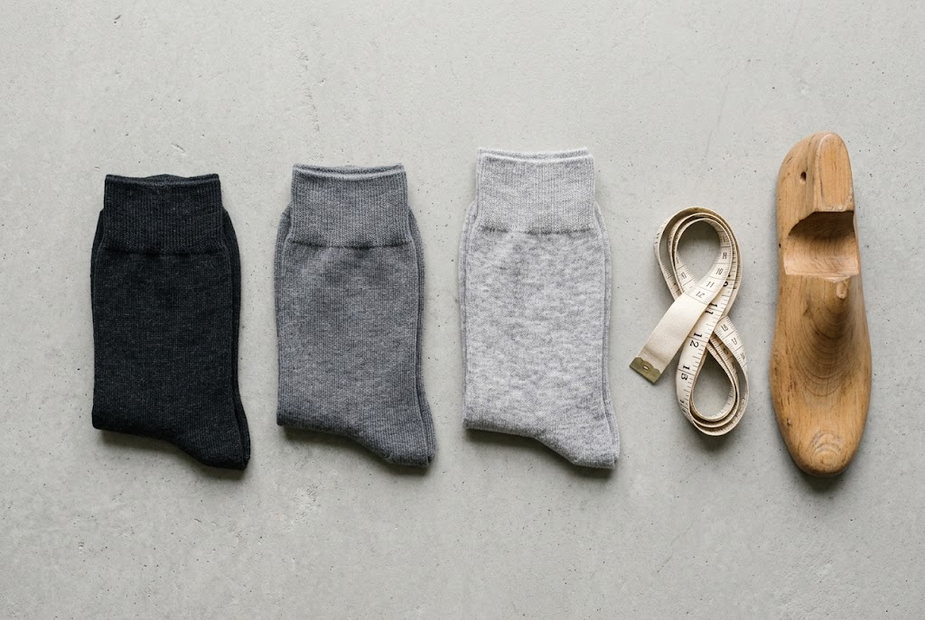Three folded pairs of socks in graded sizes in a row with a cloth tape and blocker