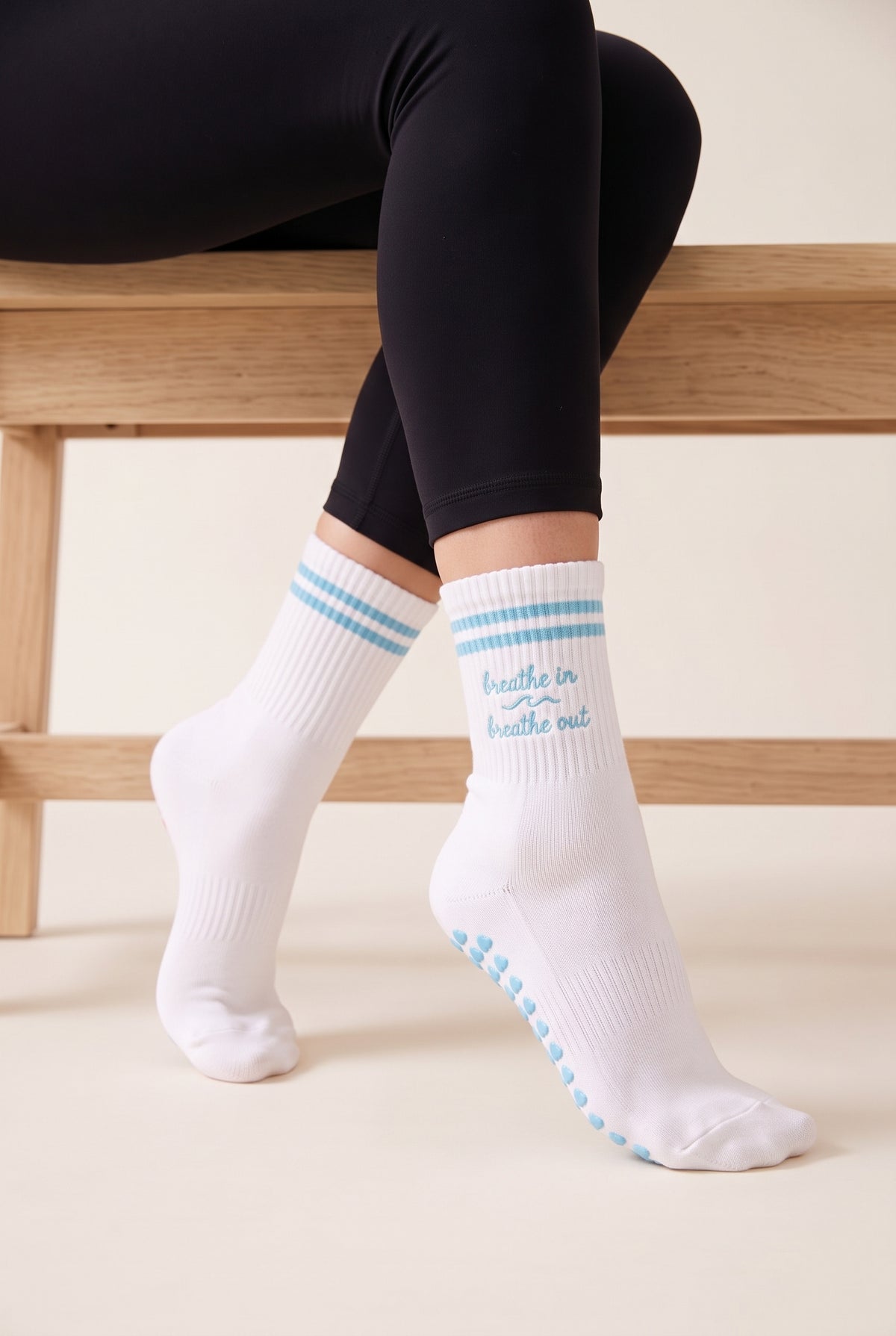 Model wearing turquoise crew pilates grip socks beside a studio bench