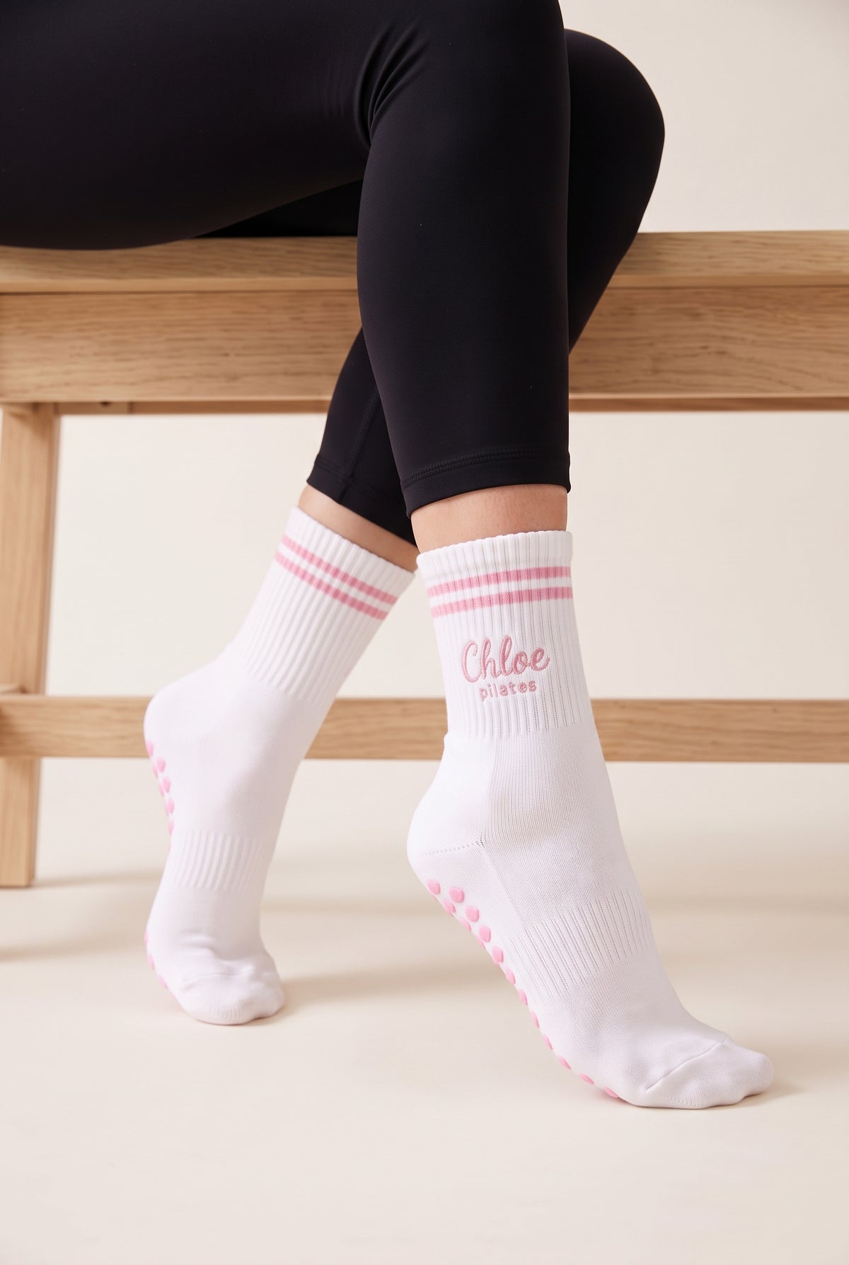 Model wearing pink crew pilates grip socks beside a studio bench