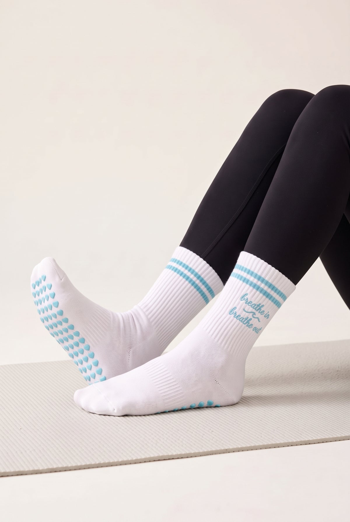 Model wearing turquoise crew pilates grip socks on a mat