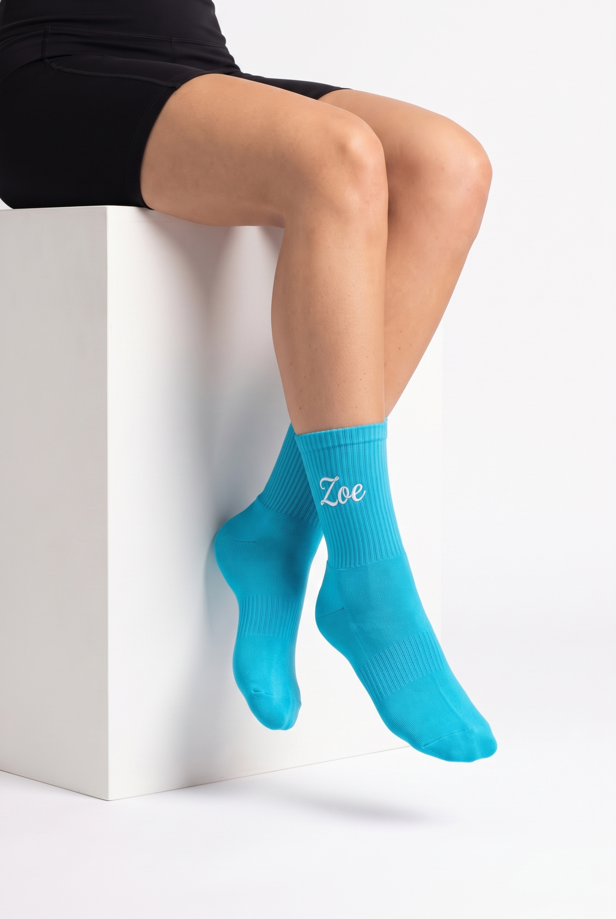 Model wearing turquoise embroidered tennis socks, seated
