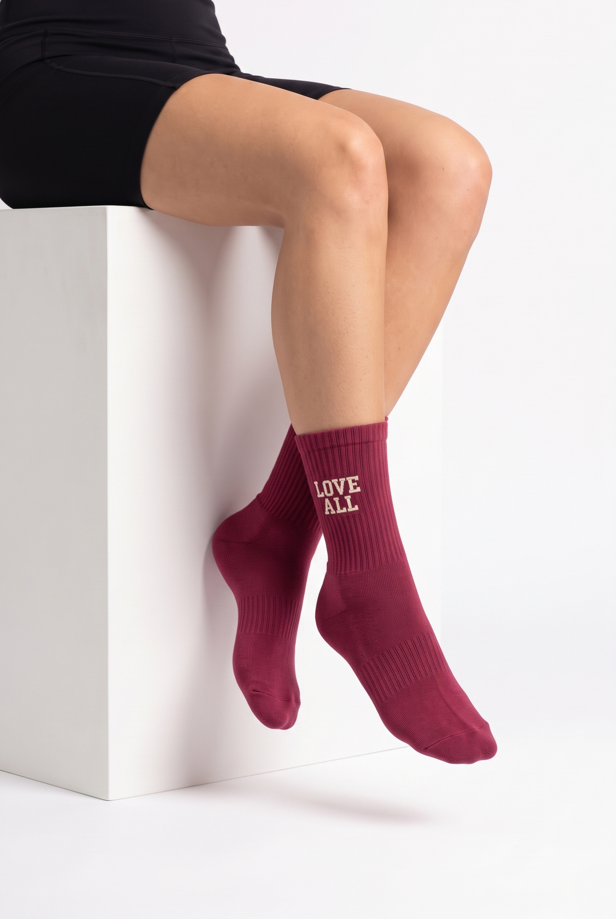 Model wearing burgundy embroidered tennis socks, seated