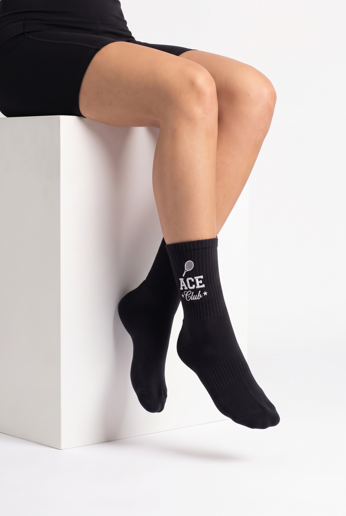 Model wearing black embroidered tennis socks, seated