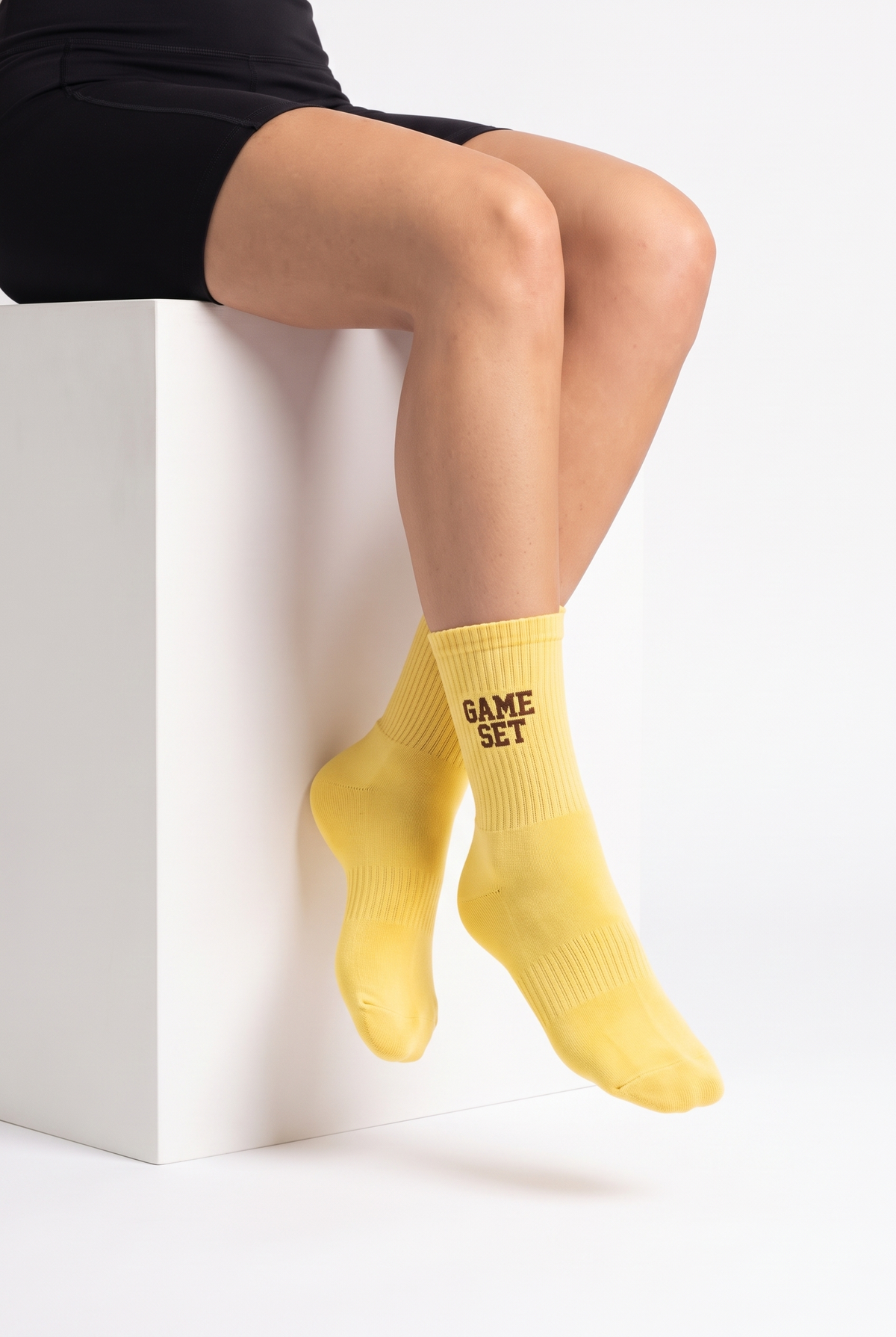 Model wearing yellow embroidered tennis socks, seated
