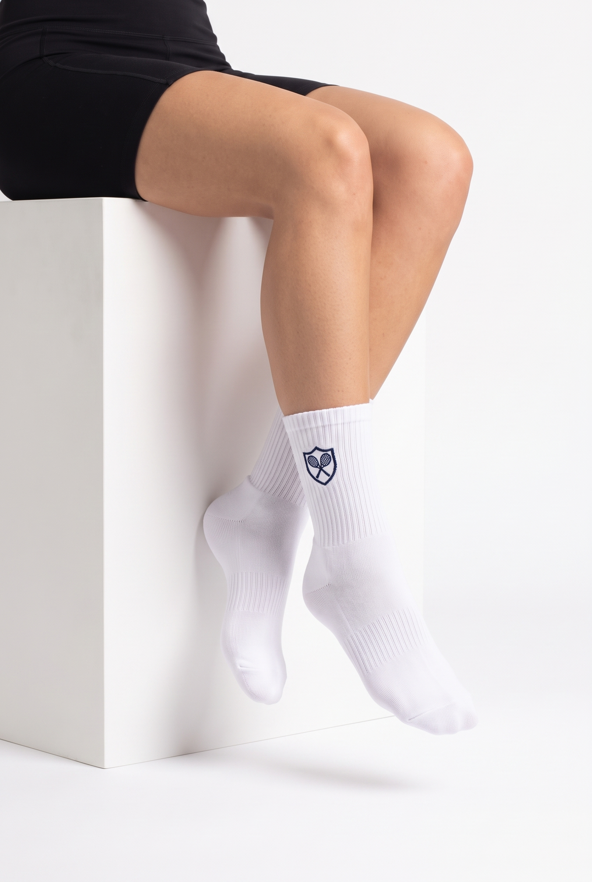 Model wearing white embroidered tennis socks, seated