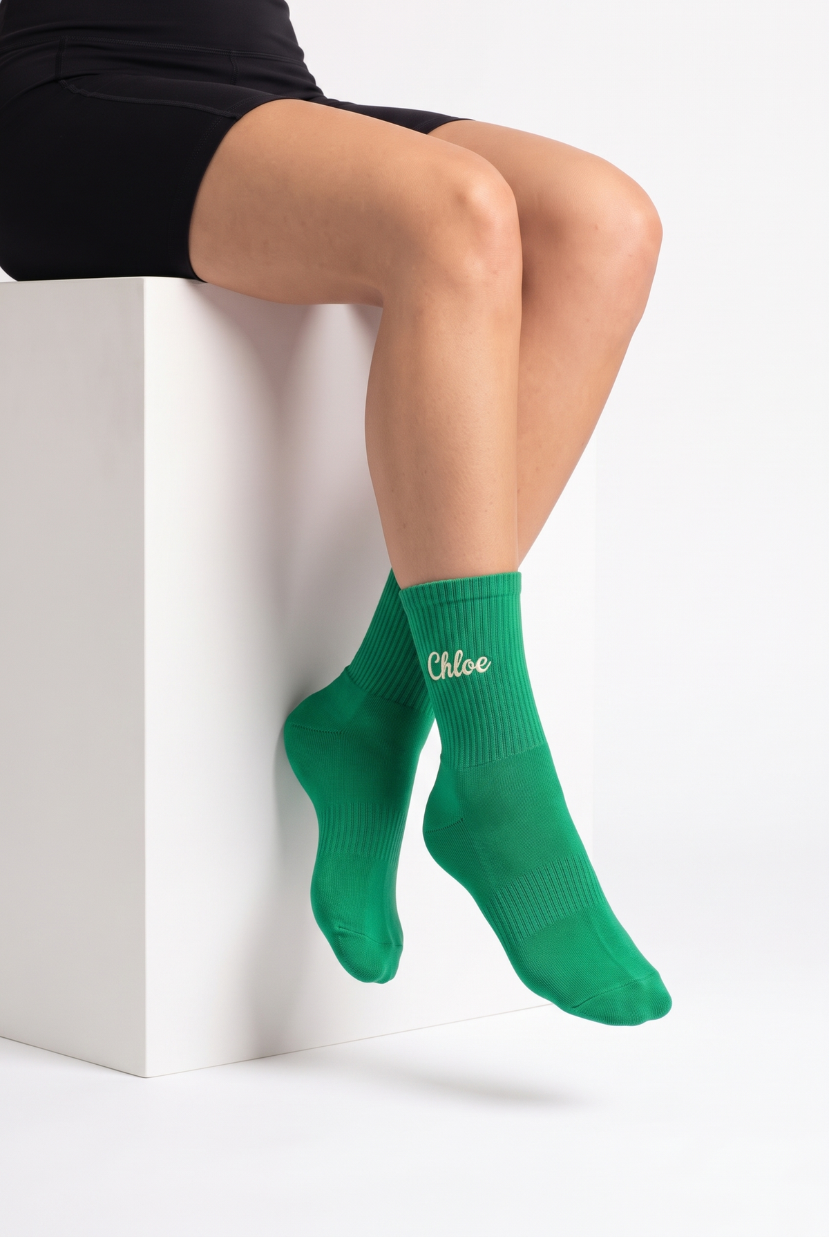 Model wearing green embroidered tennis socks, seated