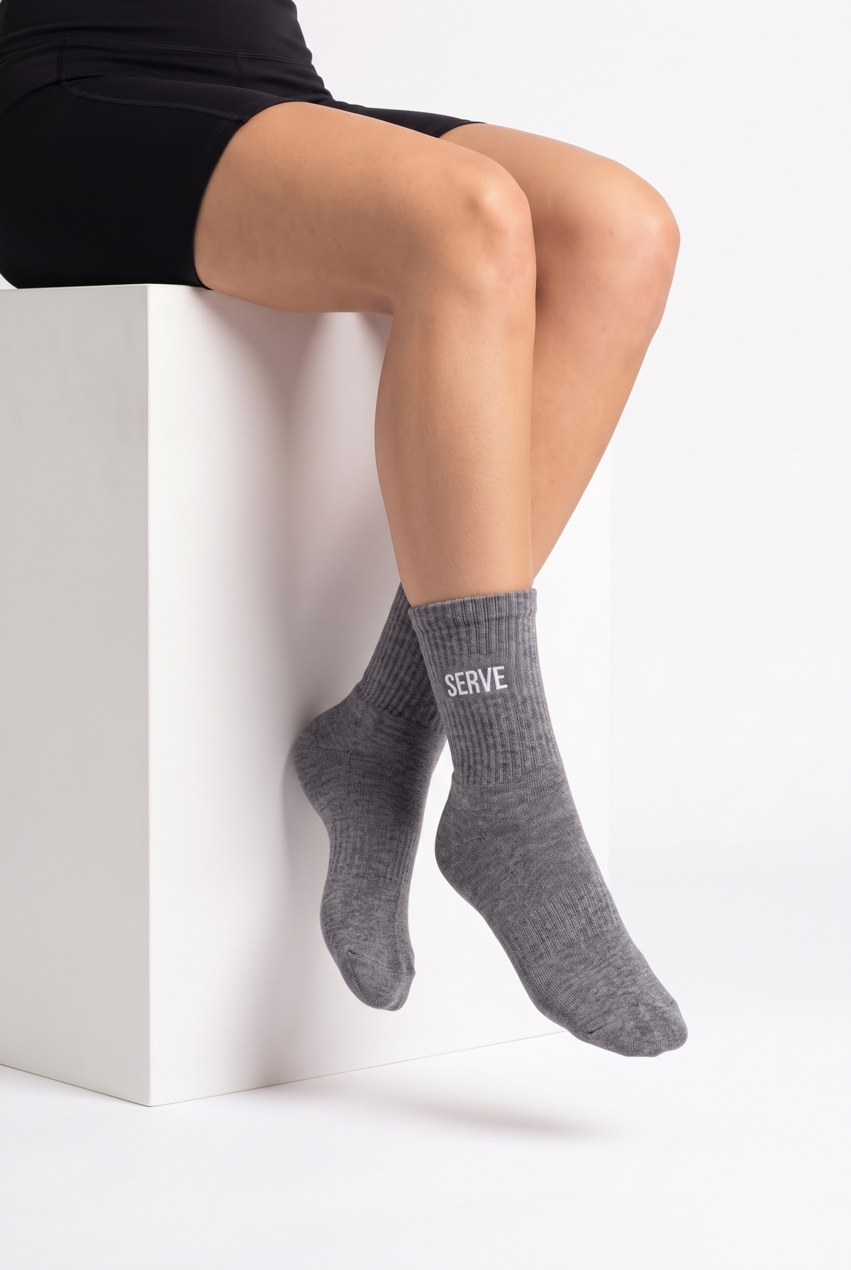Model wearing grey embroidered tennis socks, seated