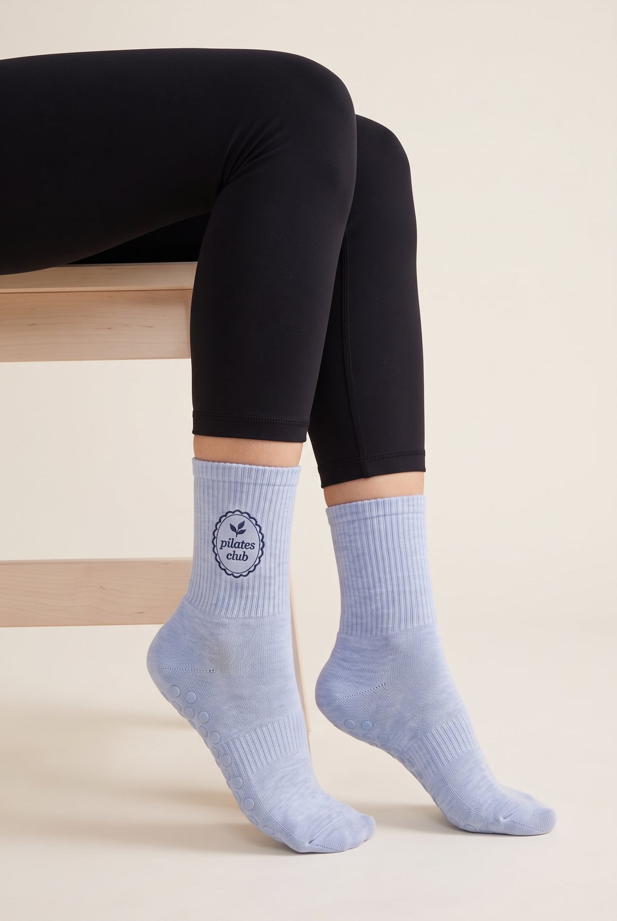 Model wearing baby blue embroidered dot grip pilates socks, seated