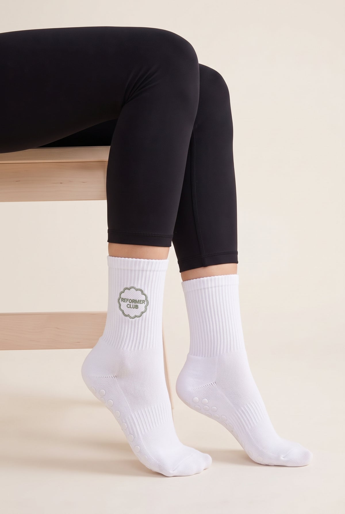 Model wearing white embroidered dot grip pilates socks, seated