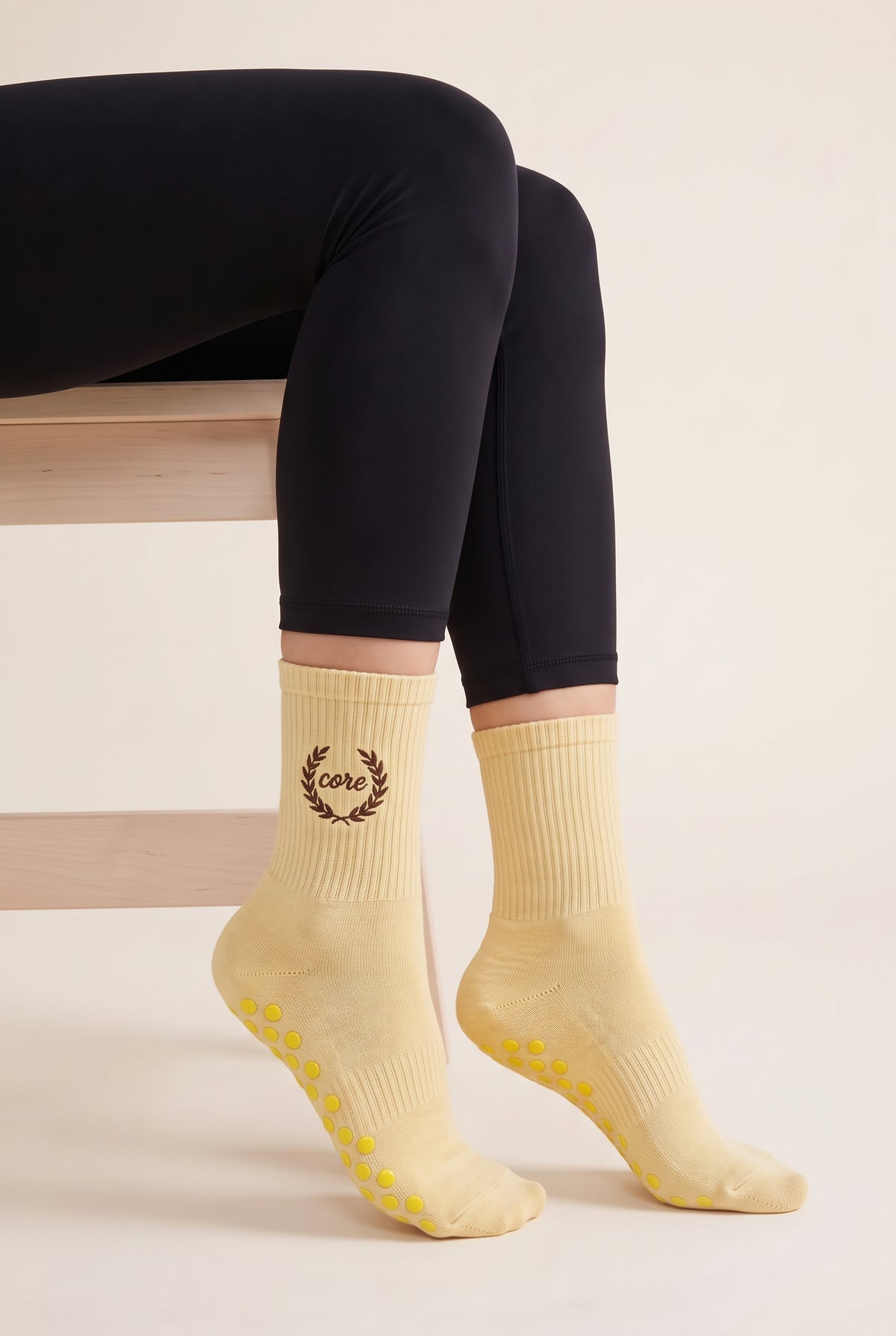 Model wearing yellow embroidered dot grip pilates socks, seated