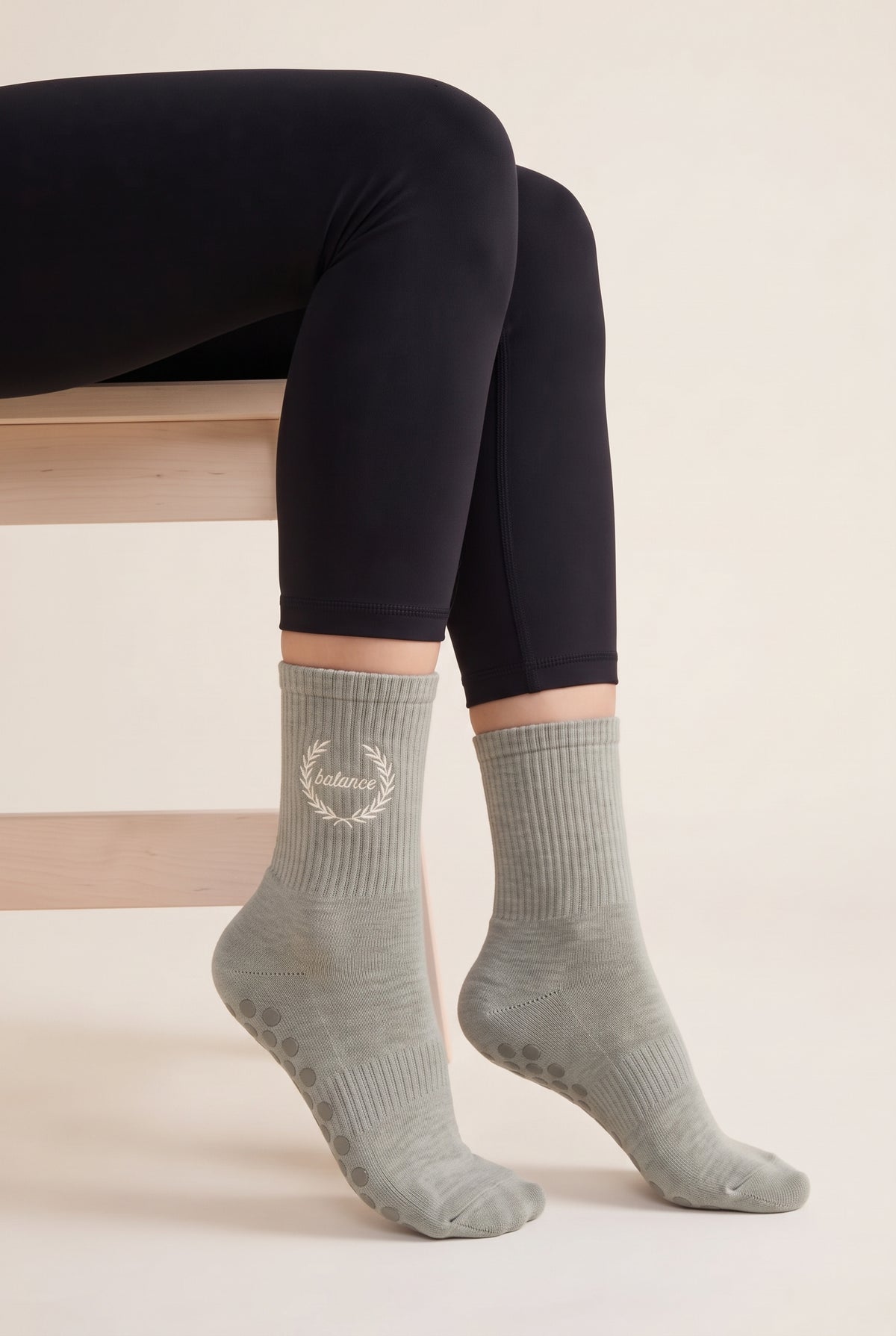 Model wearing khaki embroidered dot grip pilates socks, seated