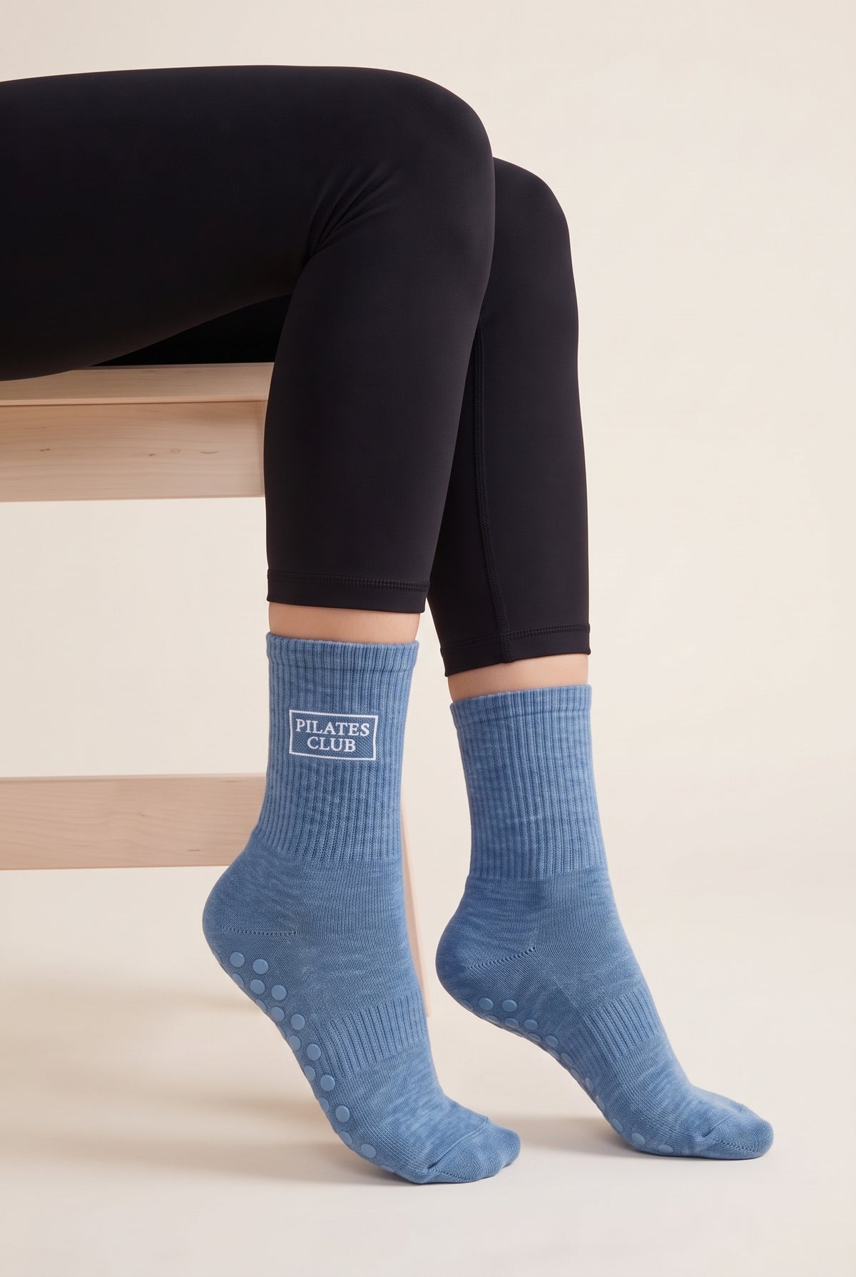 Model wearing blue embroidered dot grip pilates socks, seated