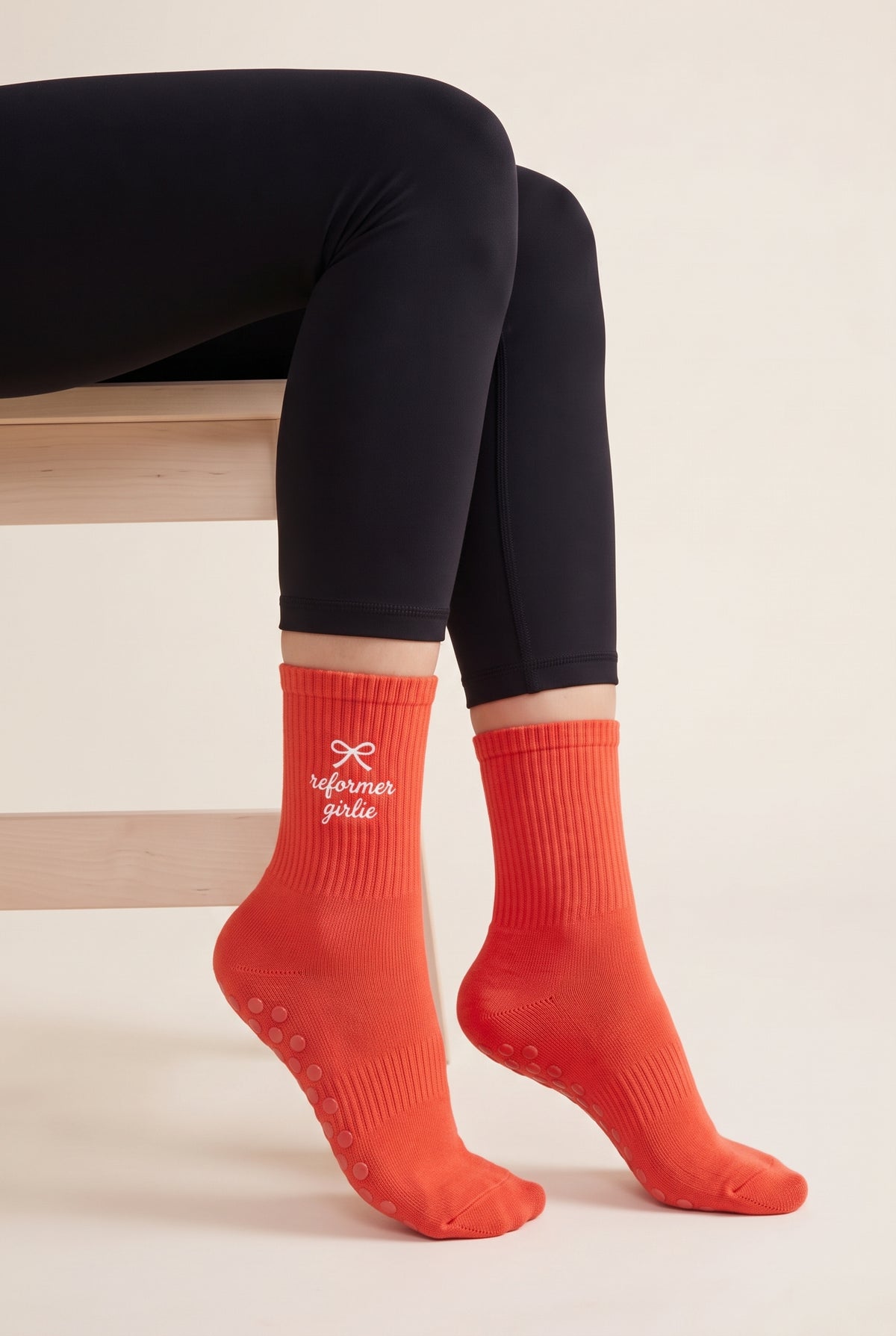 Model wearing orange embroidered dot grip pilates socks, seated