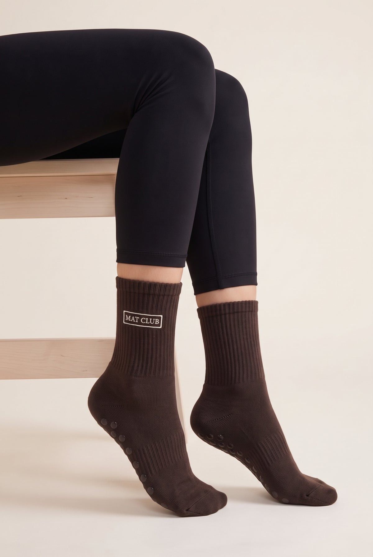 Model wearing brown embroidered dot grip pilates socks, seated