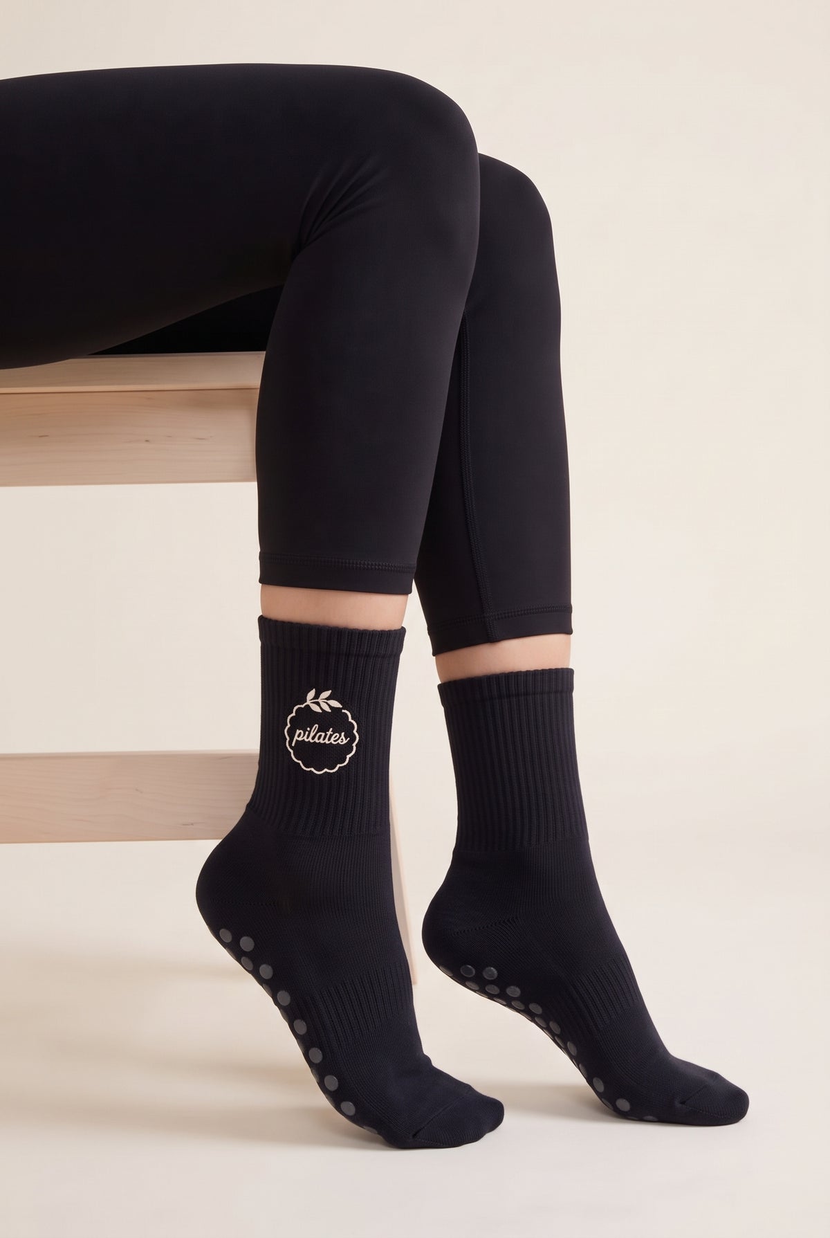 Model wearing black embroidered dot grip pilates socks, seated